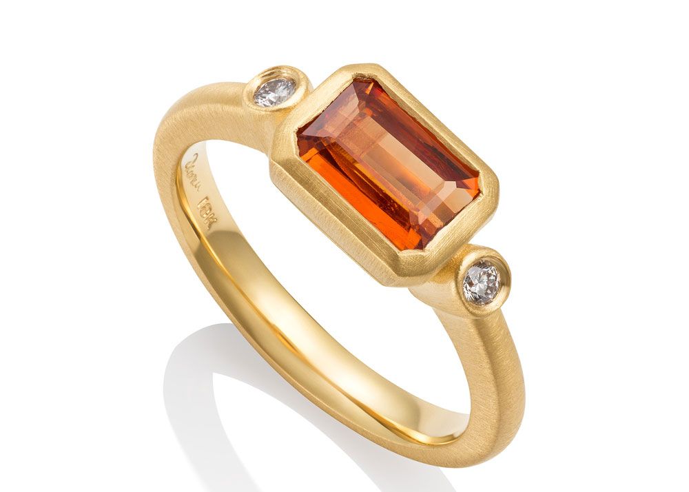 Gold ring with a large orange gemstone in the center on white background