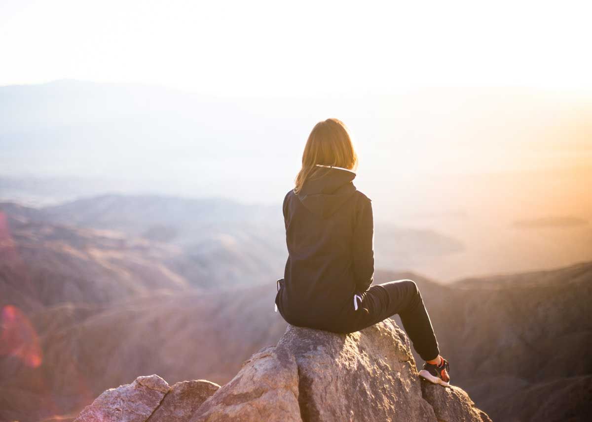 Woman sitting on top of a mountain at sunset