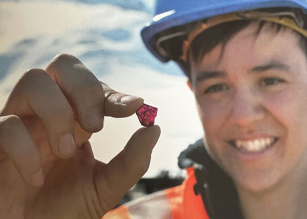 Smiling miner holding up a pink rough ruby gemstone in Greenland